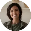 A smiling woman stands in front of a plain white wall, exuding warmth and positivity.